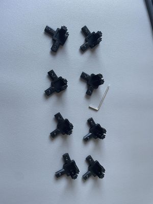 Eight black corner bracket pieces laid out on a table, with an allen key